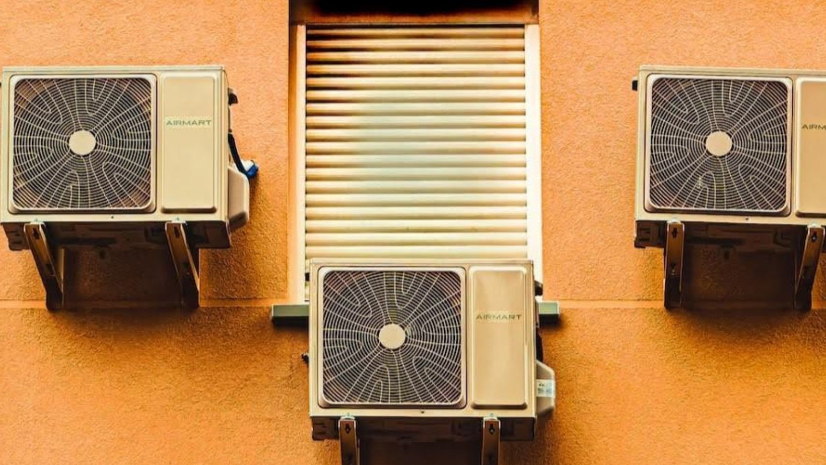 Three air conditioners and an air filter on an orange wall.