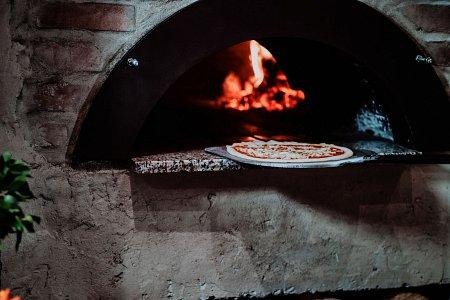 putting a pizza into a traditional masonry oven