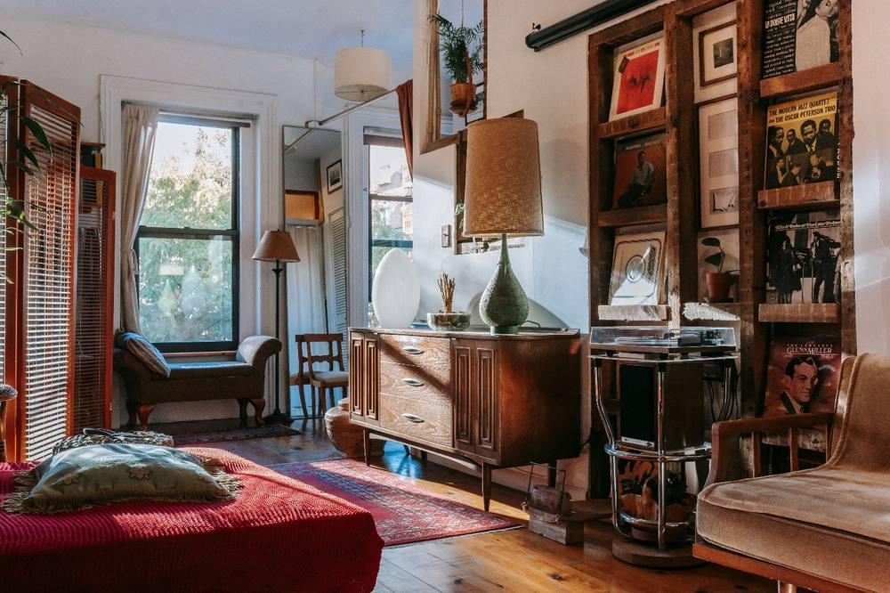 A cozy studio with a bed, couch, vintage furniture, and vinyl records, illustrating how character-rich pieces can shape the style of a modern home.